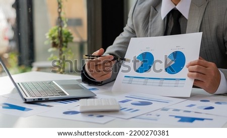 businessman holding pen and pie chart document showing company financial data He sits in a private office with a laptop analyzing financial data in chart form. financial concept