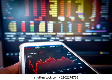 Businessman holding phone checking stock market data on computer screen background. - Shutterstock ID 2102174788