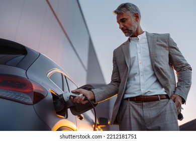 Businessman, holding power supply and charging his electric car during sunset. Concept of ecology tranport.