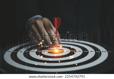 Businessman holding a red dart aiming precisely at the center of the target board and digital technology graph. business investment objective concept Marketing strategies and goals for success