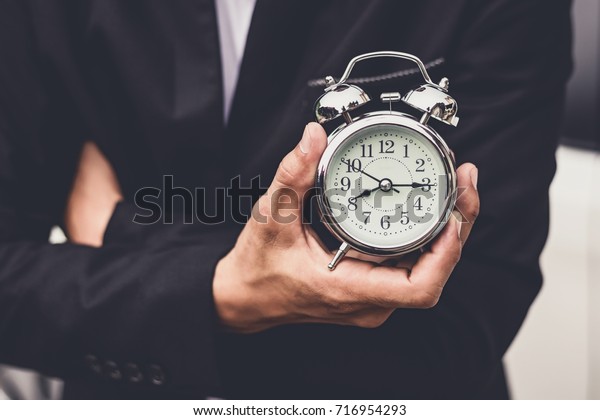 Businessman holding the retro clock in front of the\
white car