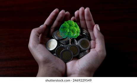 A businessman holding a small tree sprouting from a stack of money, representing financial growth and savings, with a coin in his other hand. - Powered by Shutterstock