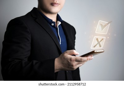 Businessman Holding Smartphone With Check Icon And Virtual Cross. Checklist And Quiz Concepts Crosses And Checkmarks, Rejection Of Wrong Answers And Correct Answers. Right Decision