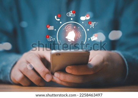 Businessman holding smartphone with virtual alarm bell ringing and social media icon include message ,letter , cloud computing and call for application notification alert concept.