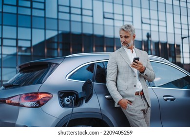 Businessman holding smartphone while charging car at electric vehicle charging station, closeup. - Powered by Shutterstock