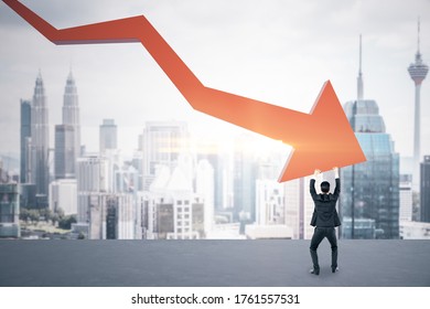 Businessman holding stock market crash red arrow on city background. Business and financial crisis concept.