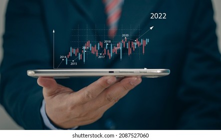 Businessman holding tablet 2022 stock market forecast outlook, charts and candlesticks, stock market movement trend, past to present. - Shutterstock ID 2087527060
