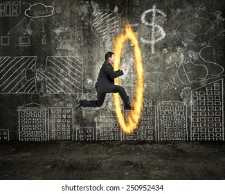 Businessman holding tablet jumping through fire hoop with doodles wall background
