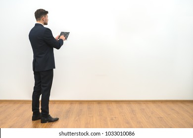 The businessman holding a tablet on the white wall background - Powered by Shutterstock