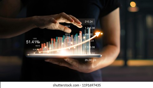 Businessman holding tablet and showing a growing virtual hologram of statistics, graph and chart with arrow up on dark background. Stock market. Business growth, planing and strategy concept.  - Shutterstock ID 1191697435