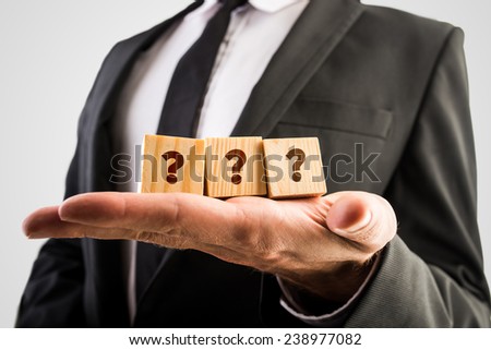Businessman holding three wooden cubes displaying question marks.