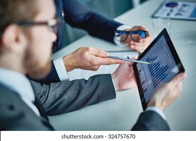 Businessman holding touchpad with data being explained by his colleague