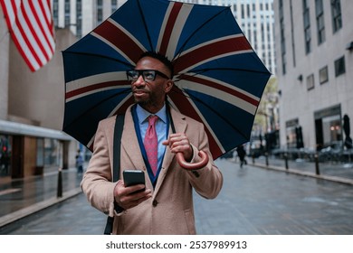 Businessman holding a union jack umbrella and using a smart phone while walking down a new york city street - Powered by Shutterstock