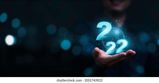 Businessman holding virtual 2022 number with blue bokeh background and copy space for merry Christmas and happy new year concept.