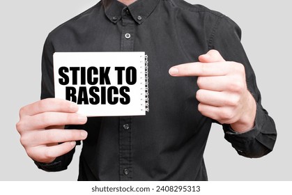Businessman holding a white notepad with text STICK TO BASICS, business concept