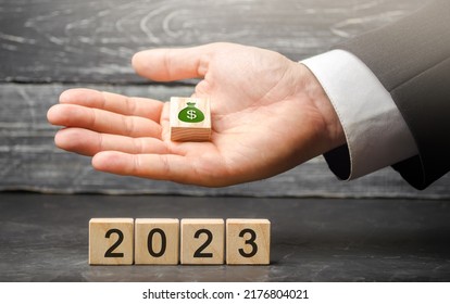 Businessman Holding Wood Blocks With Dollars Money And 2023. Budget Planning Concept. Financial Goals And Plans. Business And Finance Concept. Forecasting And Analysis. Investments. Vision