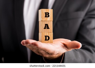 Businessman holding wooden alphabet blocks reading - Bad - balanced in the palm of his hand in a conceptual image, closeup view.