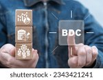 Businessman holding wooden blocks with icons and sees virtual button with abbreviation: BDC. Concept of BDC Business Development Company.