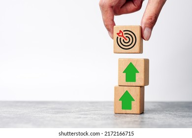 Businessman holding wooden cube with target board icon and arrow on wooden table. Goals and planning for success in marketing business, achieve the objective concept. copy space               