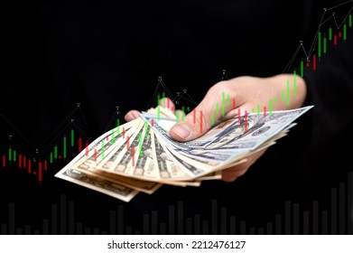 A Businessman Holds Banknotes And Investments In His Hand, As Well As A Currency Exchange Chart, A Stock Market Chart, Online Banking Technologies.