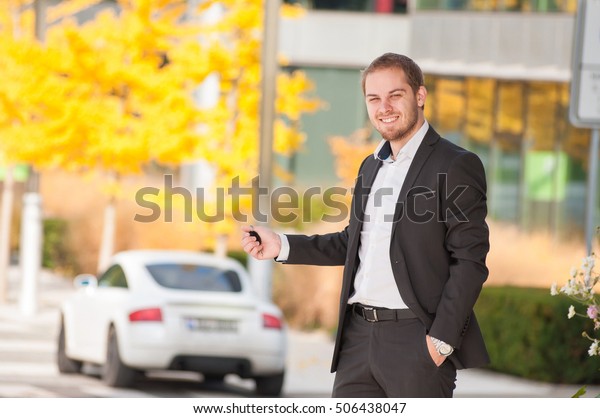 Businessman holds car keys in\
front of his car. Man in suit holding car keys from his white sport\
car.