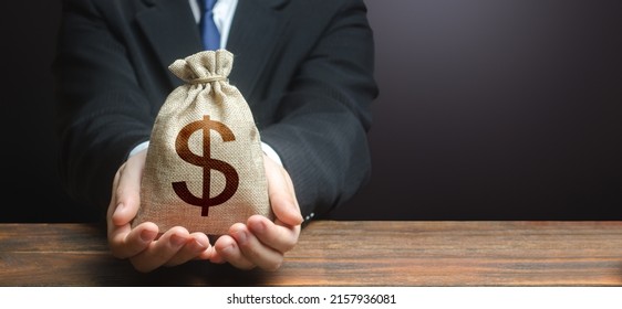 Businessman Holds Out Dollar Money Bag. Getting A Grant. Mortgage, Loan Approval. Easy Money. Salary, Benefits, Profit. Attracting Investments. Deposit Savings. Cashback. Banking And Crediting.