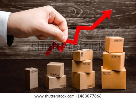 Businessman holds a red arrow up above cardboard boxes folded incrementally. Increase sales and production rate of goods and products. Profit growth, business development. Increase in export volumes.