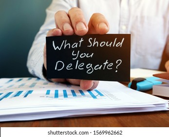 Businessman holds sign What Should You Delegate. Delegation concept.