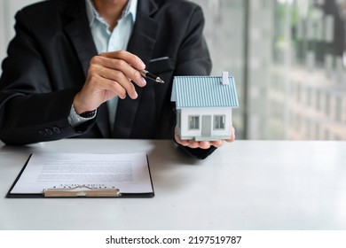 Businessman Or Home Insurance Broker Holding A Small Model House Offers Home Insurance. House Trading