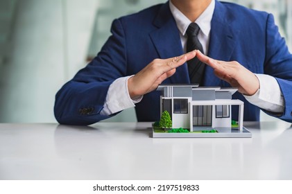 Businessman Or Home Insurance Broker Holding A Small Model House Offers Home Insurance. House Trading