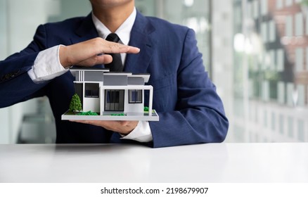 Businessman Or Home Insurance Broker Holding A Small Model House Offers Home Insurance. House Trading