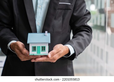 Businessman Or Home Insurance Broker Holding A Small Model House Offers Home Insurance. House Trading