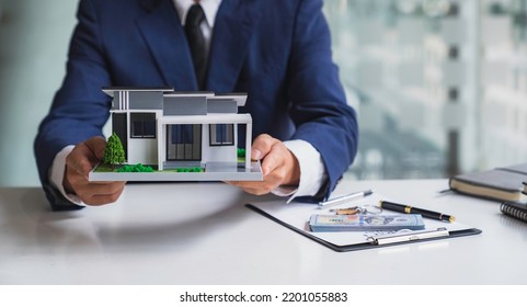 Businessman Or Home Insurance Broker Holding A Small Model House Offers Home Insurance. House Trading