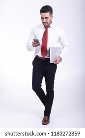 Businessman Isolated. Handsome Young Indian Businessman Holding Laptop, Looking At His Phone, Thinking Looks. Full Length Shot.