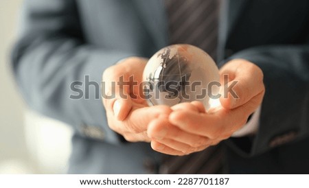 Businessman in jacket holding glass ball with world map closeup