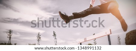 Businessman jumping a hurdle while running on the racing track
