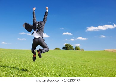 Businessman jumping for joy celebrating a successful achievement in a lush green field under a blue sky