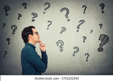 Businessman keeps hand under chin, thoughtful gesture, looking ahead focused, thinking answers to different questions in his head. Interrogation mark symbols. Pensive student pondering of solutions. - Powered by Shutterstock