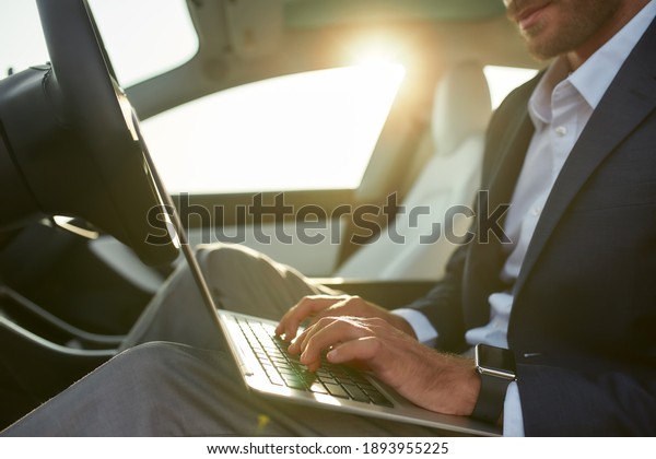 Businessman with laptop sitting on\
driver seat in luxury car, cropped. Success and lifestyle\
concept