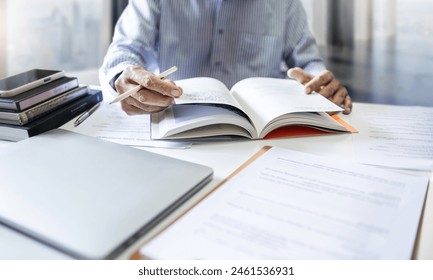 Businessman, lawyer, legal advisor, working with laptop and reading legal processing books for accuracy in contract documents reviewing business contracts before giving advice to customers - Powered by Shutterstock