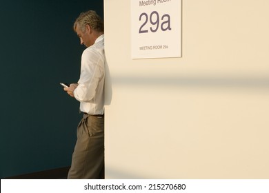 Businessman Leaning Against Wall Outside Meeting Room, Making Private Call On Mobile Phone, Side View