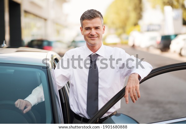 Businessman leaning on the car door and\
smiling at camera, dealership and business\
concept