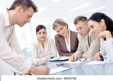 Businessman leaning on desk, explaining to four colleagues sitting.