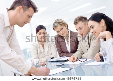 Businessman leaning on desk, explaining to four colleagues sitting.