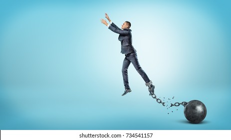 A Businessman Leaps Up With Outstretched Hands While He's Chained To An Iron Ball With A Broken Link. Breaking Boundaries. Reach Your Goal. Business Restrictions.