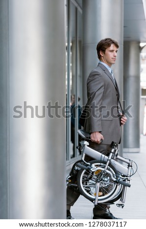 Businessman leaving office building carrying folding commuter bicycle