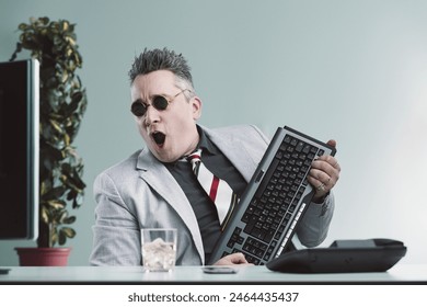 Businessman in a light grey suit playfully imitates a guitar player using his computer keyboard, full of enthusiasm - Powered by Shutterstock