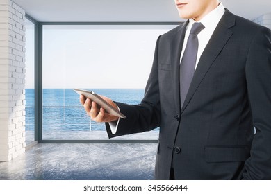 Businessman looking at digital tablet in empty loft room with ocean view - Shutterstock ID 345566444