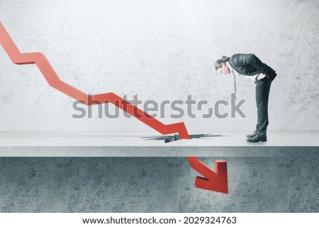 Businessman looking down at falling red arrow breaking through concrete ground. Crisis and economic recession concept