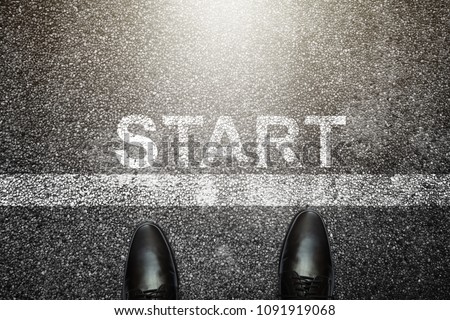 Businessman is looking down at his feet on a Asphalt road with start letters painted on the surface. An image of a milestone roadmap is a representation of success in the future goal